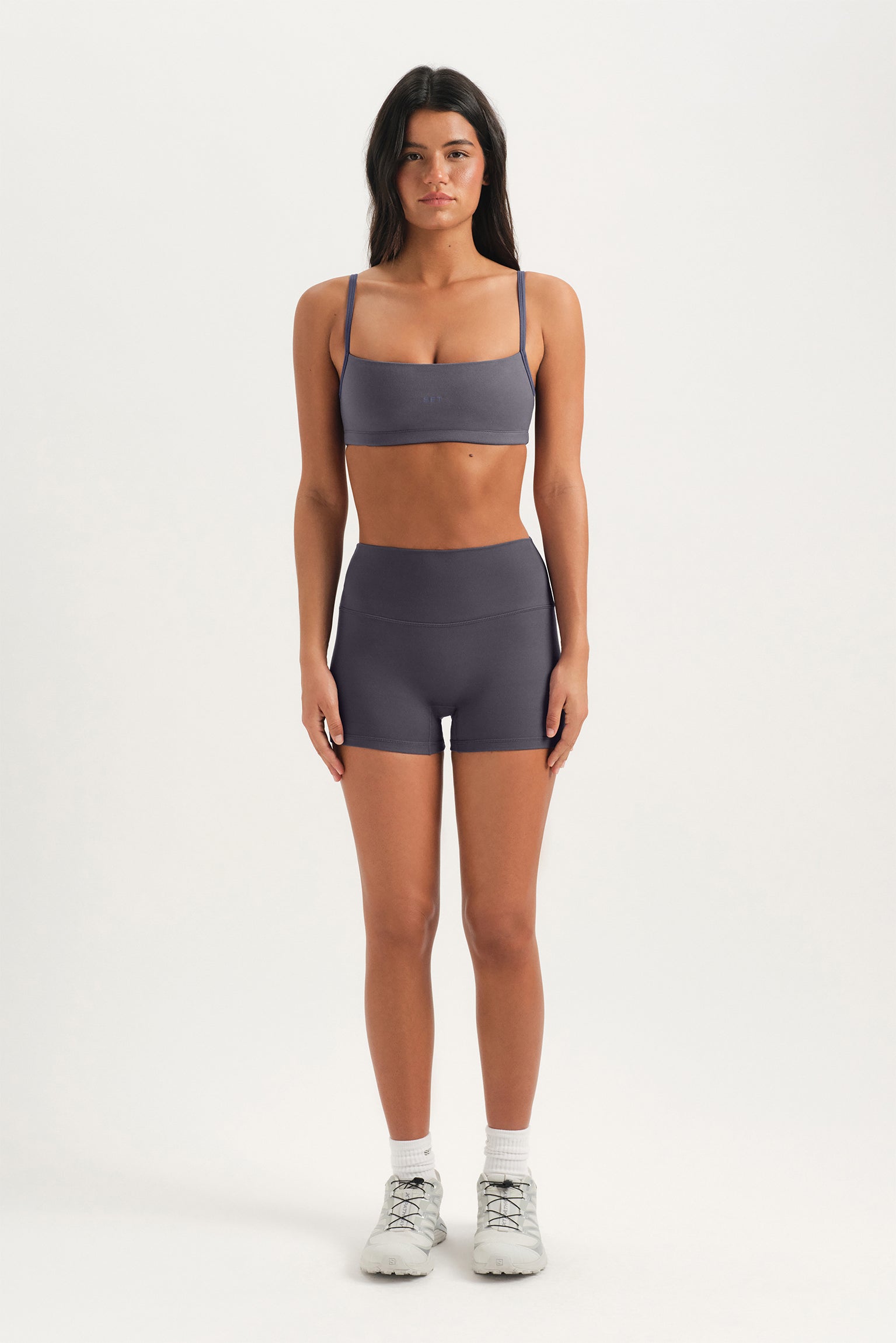 Woman wearing a gray sports bra and shorts on a white background