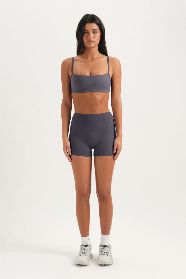 Woman wearing a gray sports bra and shorts on a white background