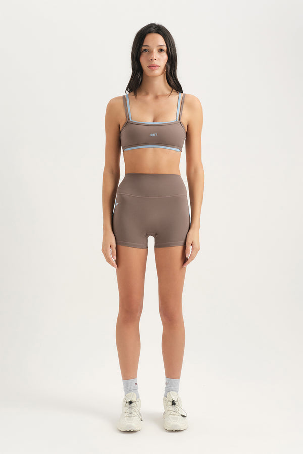 Woman wearing a brown sports bra and shorts set on a white background