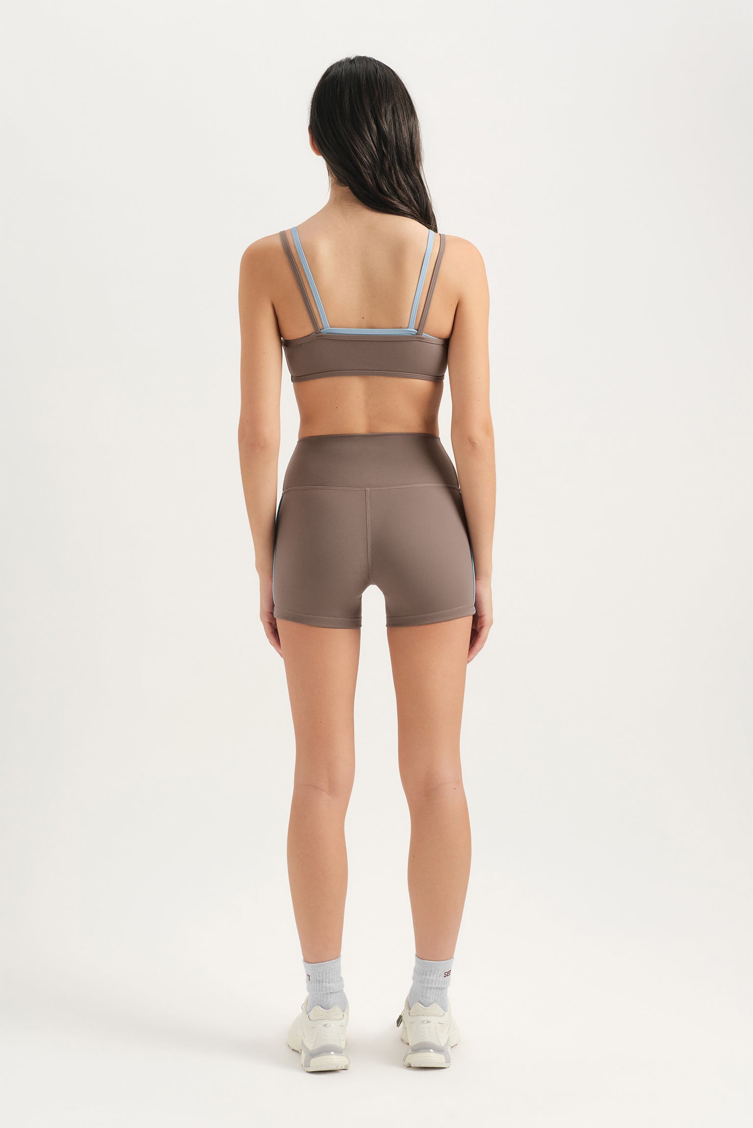 Woman wearing a brown sports bra and shorts set on a white background