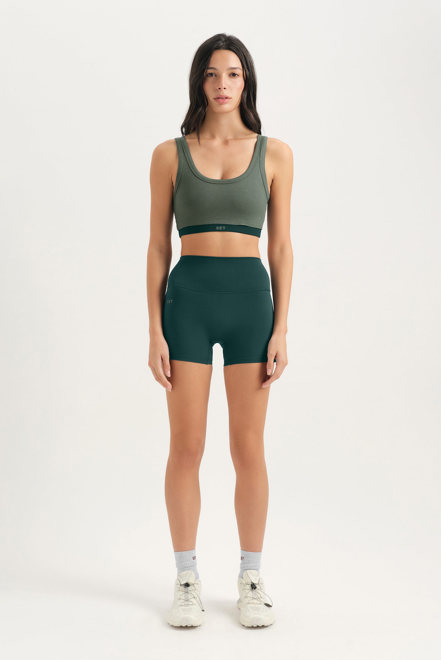 Woman wearing a green sports bra and shorts set on a white background