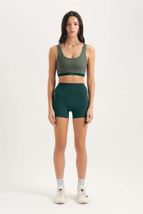 Woman wearing a green sports bra and shorts set on a white background