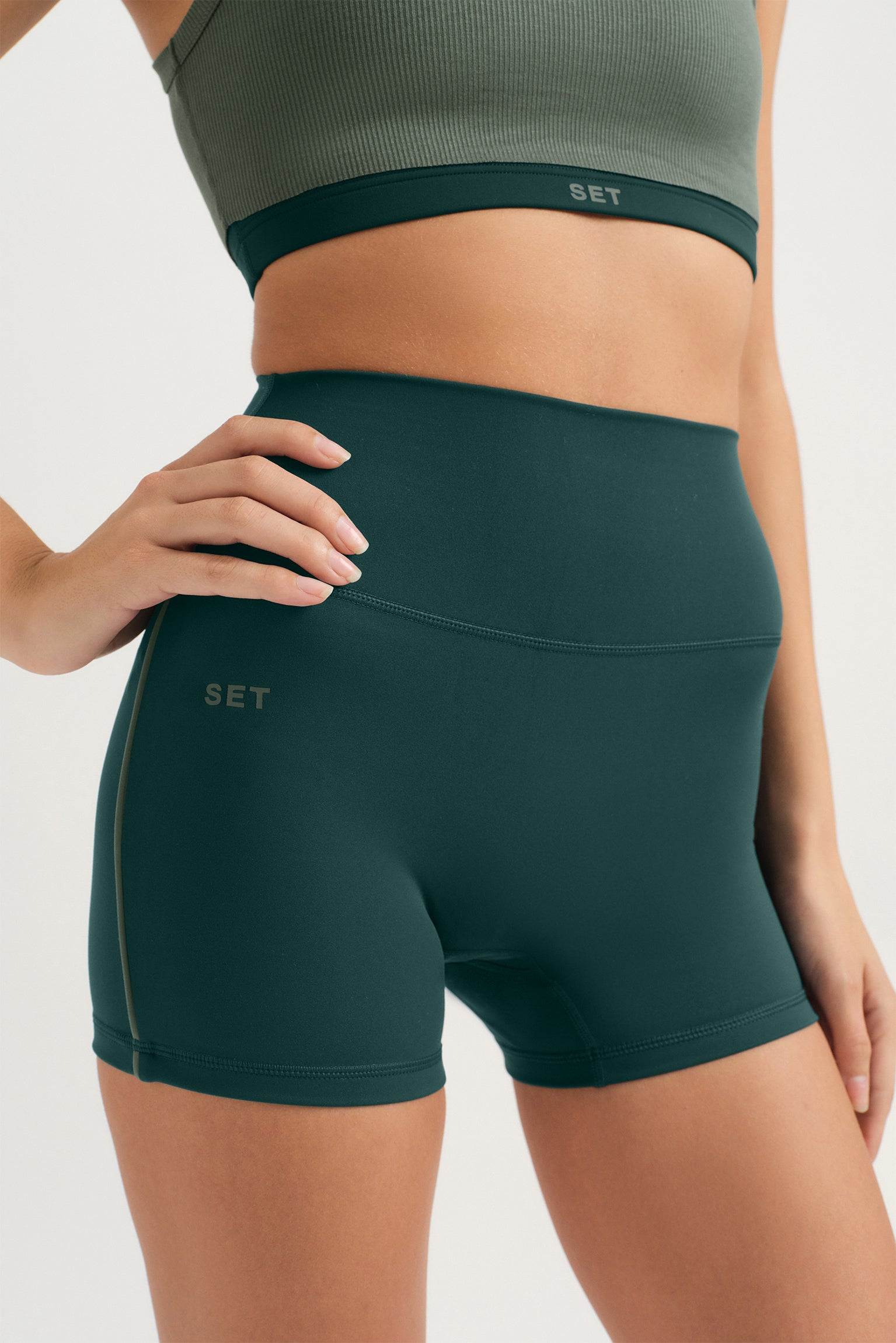 Person wearing green athletic shorts and top with 'SET' branding on a light background