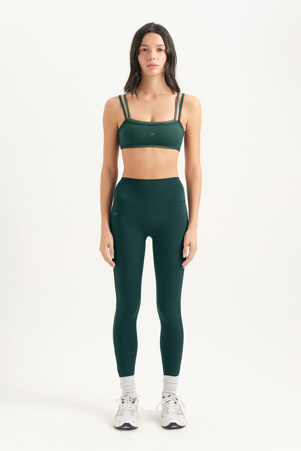 Woman wearing a green sports bra and leggings set on a white background