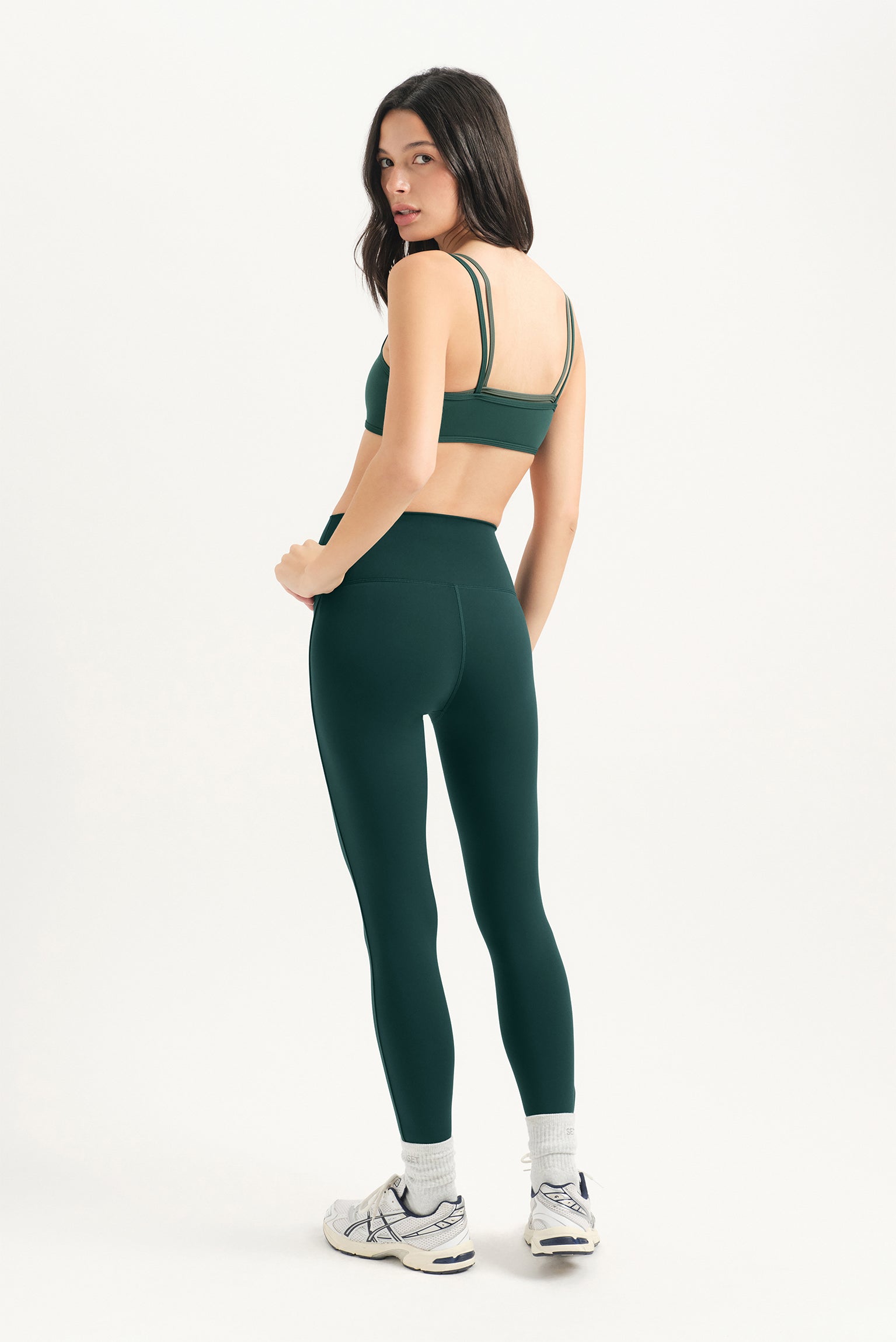 Woman wearing a green sports bra and leggings set on a white background