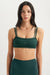 Woman wearing a green sports bra and leggings with a white background <model-info>Casey wears a size S and is 5’9”, 24” waist, 32B bust.</model-info>