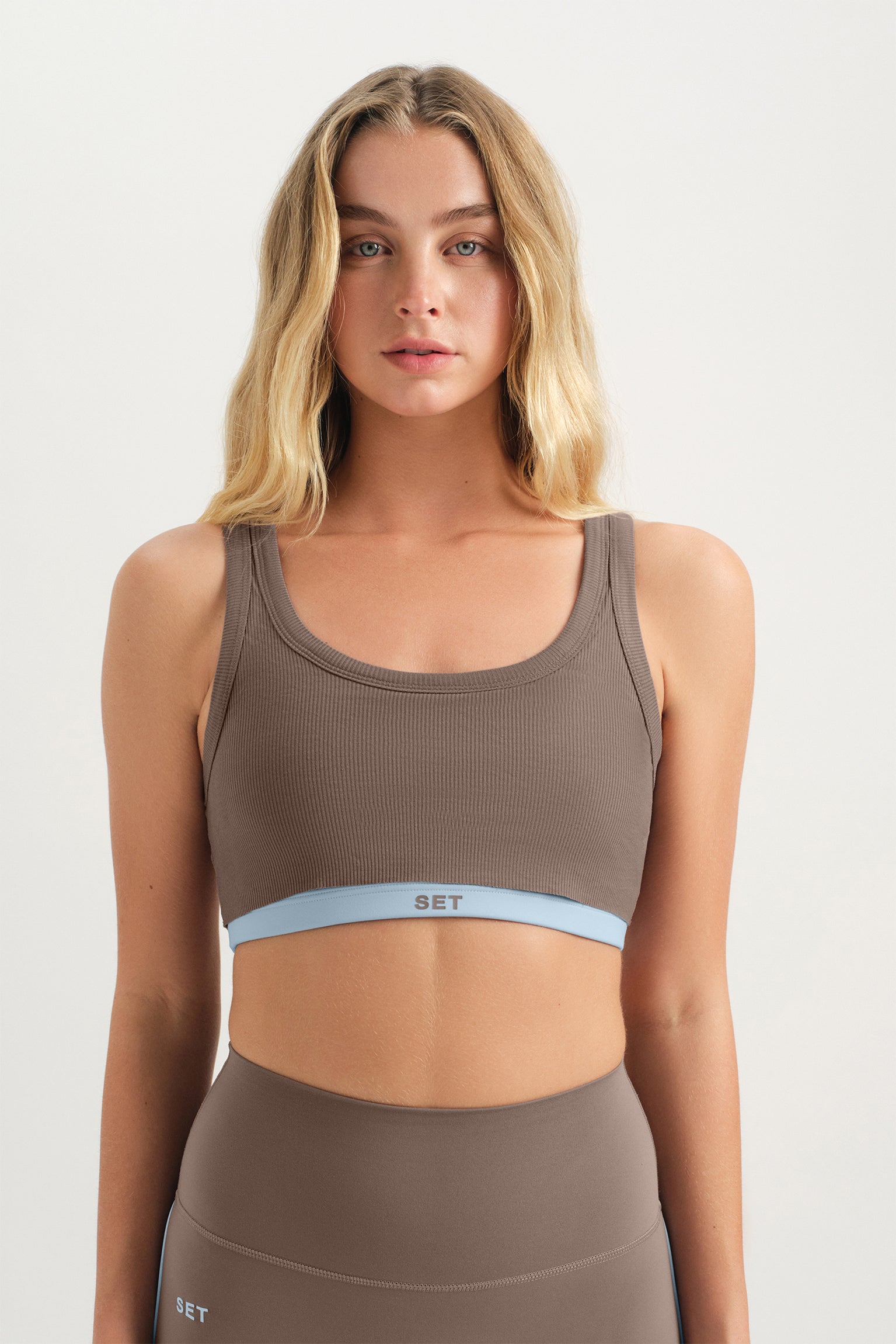 Woman wearing a brown sports bra and leggings on a white background <model-info>Grace wears a size XS and is 5'8", 25" waist, 32" bust.</model-info>