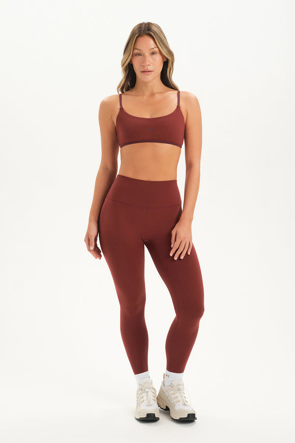 Woman wearing a maroon sports bra and leggings set on a white background