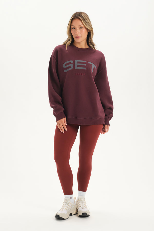 Woman wearing a maroon 'SET' sweatshirt and leggings on a white background