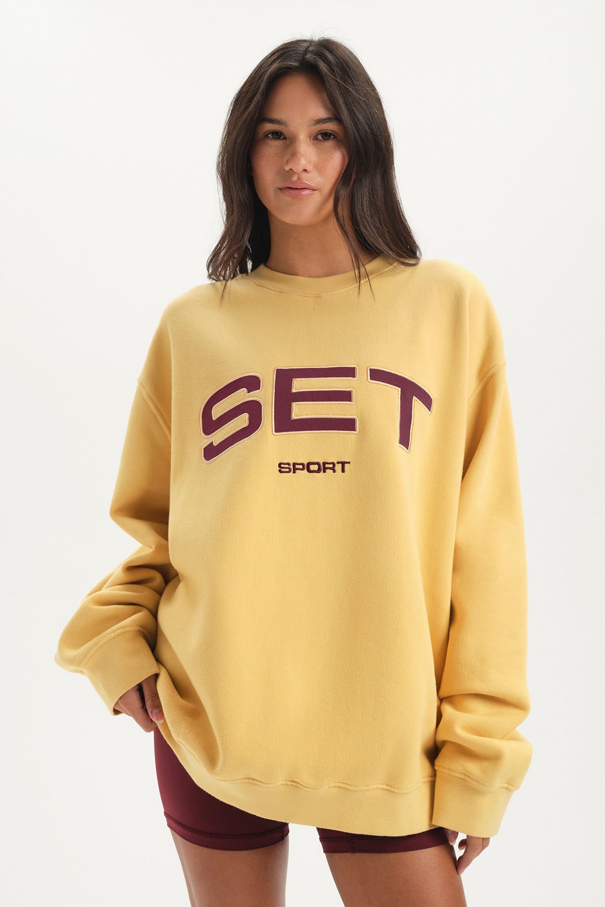 Woman wearing a yellow sweatshirt with 'SET Sport' text on a white background 