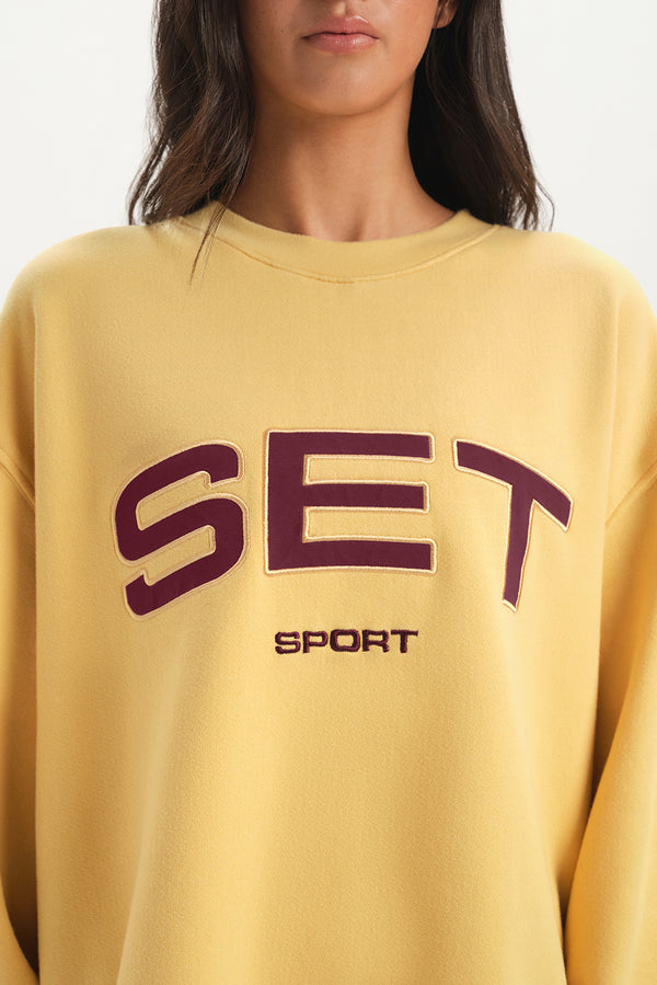Yellow sweatshirt with 'SET Sport' text worn by a person