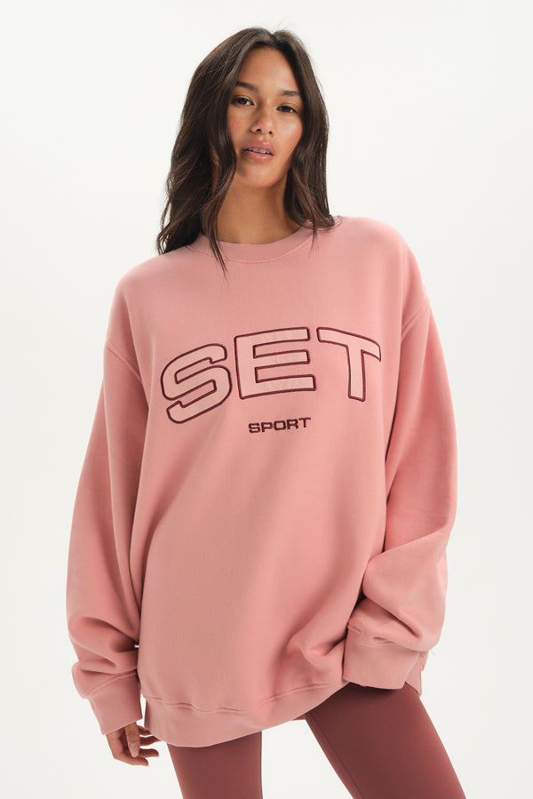 Woman wearing a pink sweatshirt with 'SET Sport' text on a white background 