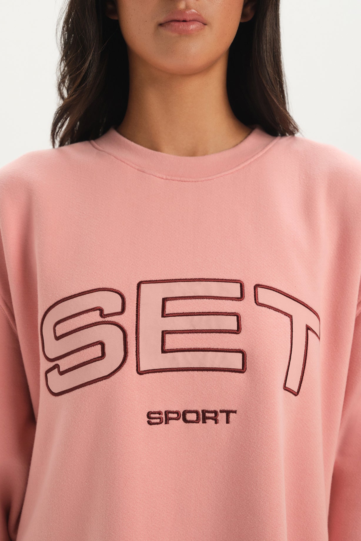 Pink sweatshirt with 'SET SPORT' text worn by a person