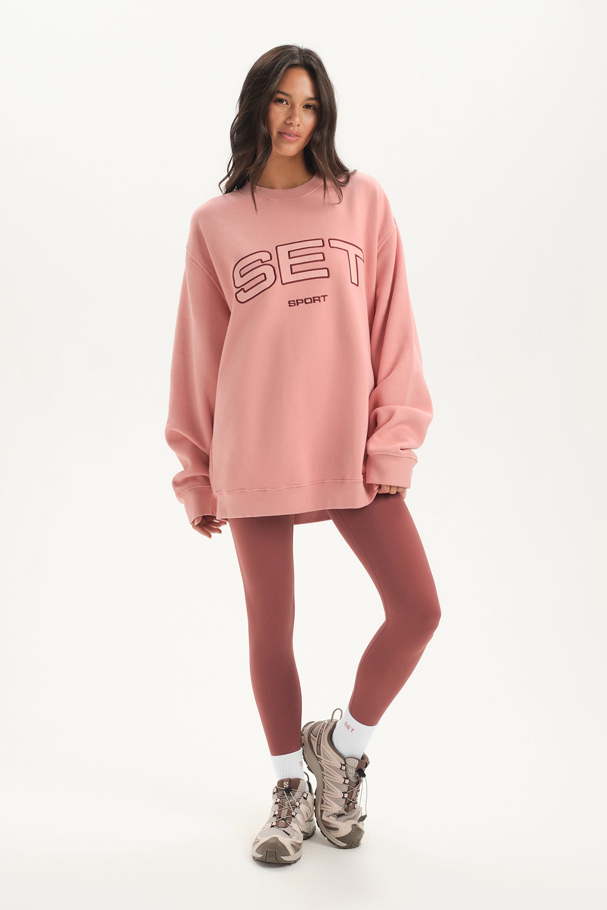 Woman wearing a pink 'SET' oversized sweatshirt and leggings on a white background