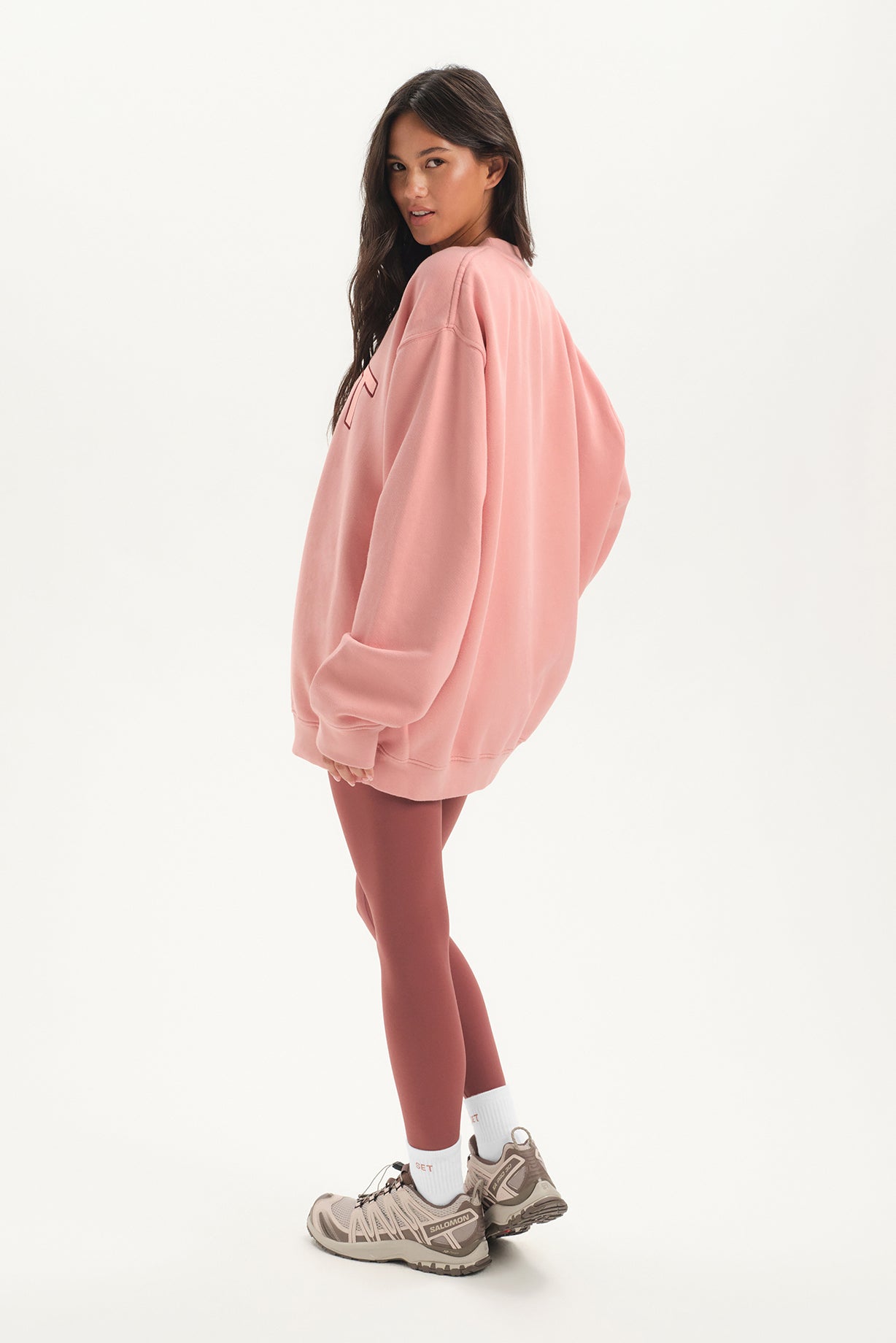 Woman wearing a pink oversized sweatshirt and leggings on a white background