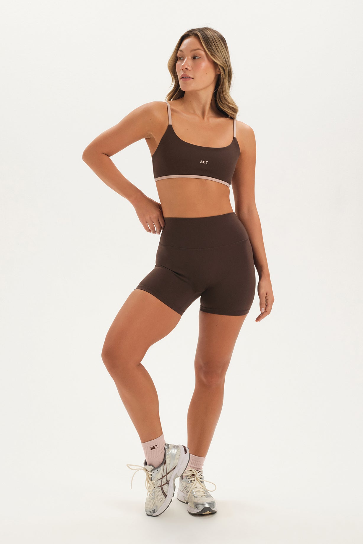Woman wearing a brown sports bra and shorts set on a white background