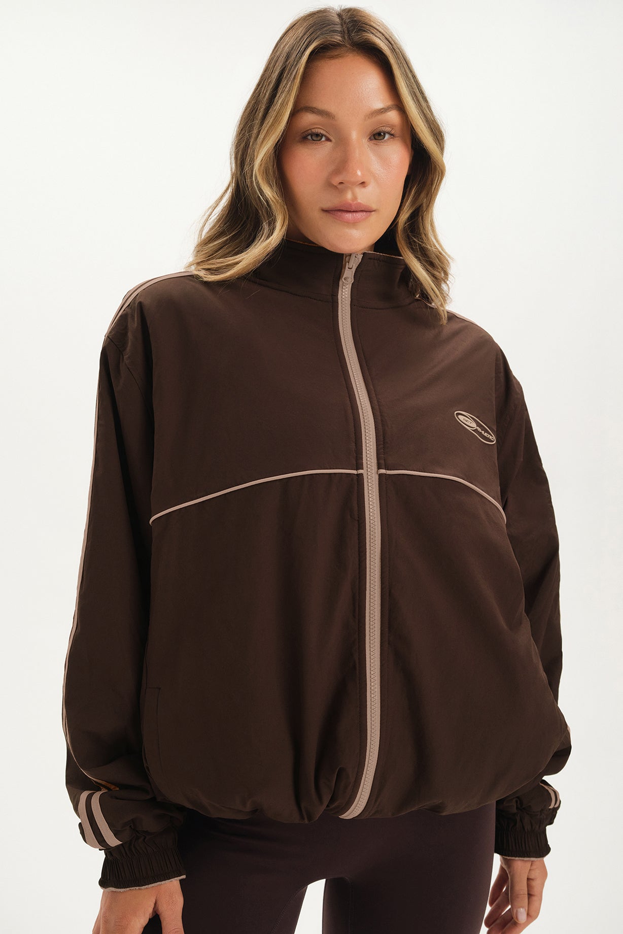 Woman wearing a brown jacket with a white zipper on a white background <model-info>Bre wears a size M and is 5’7”, 25½" waist, 33” bust.</model-info>