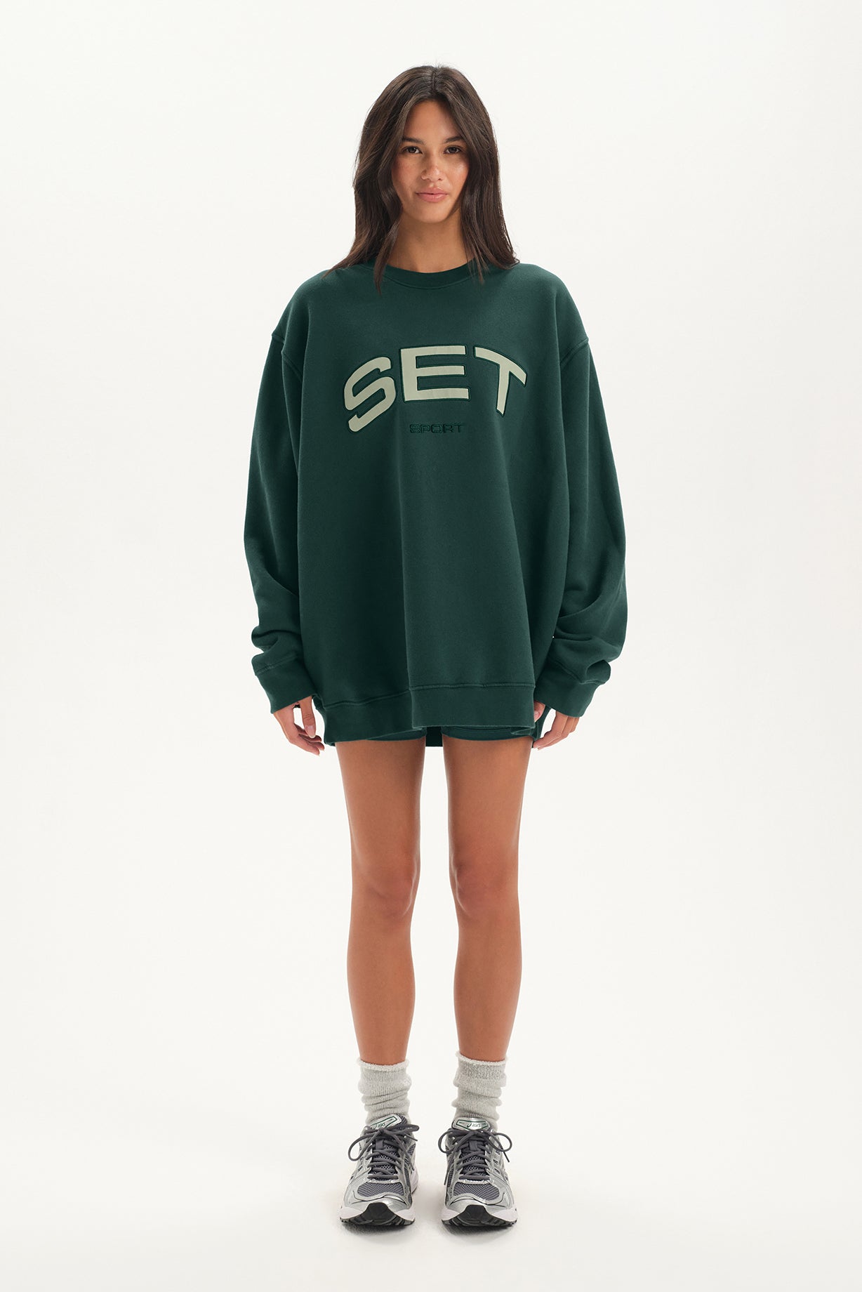 Person wearing a green sweatshirt with 'SET' logo on a white background