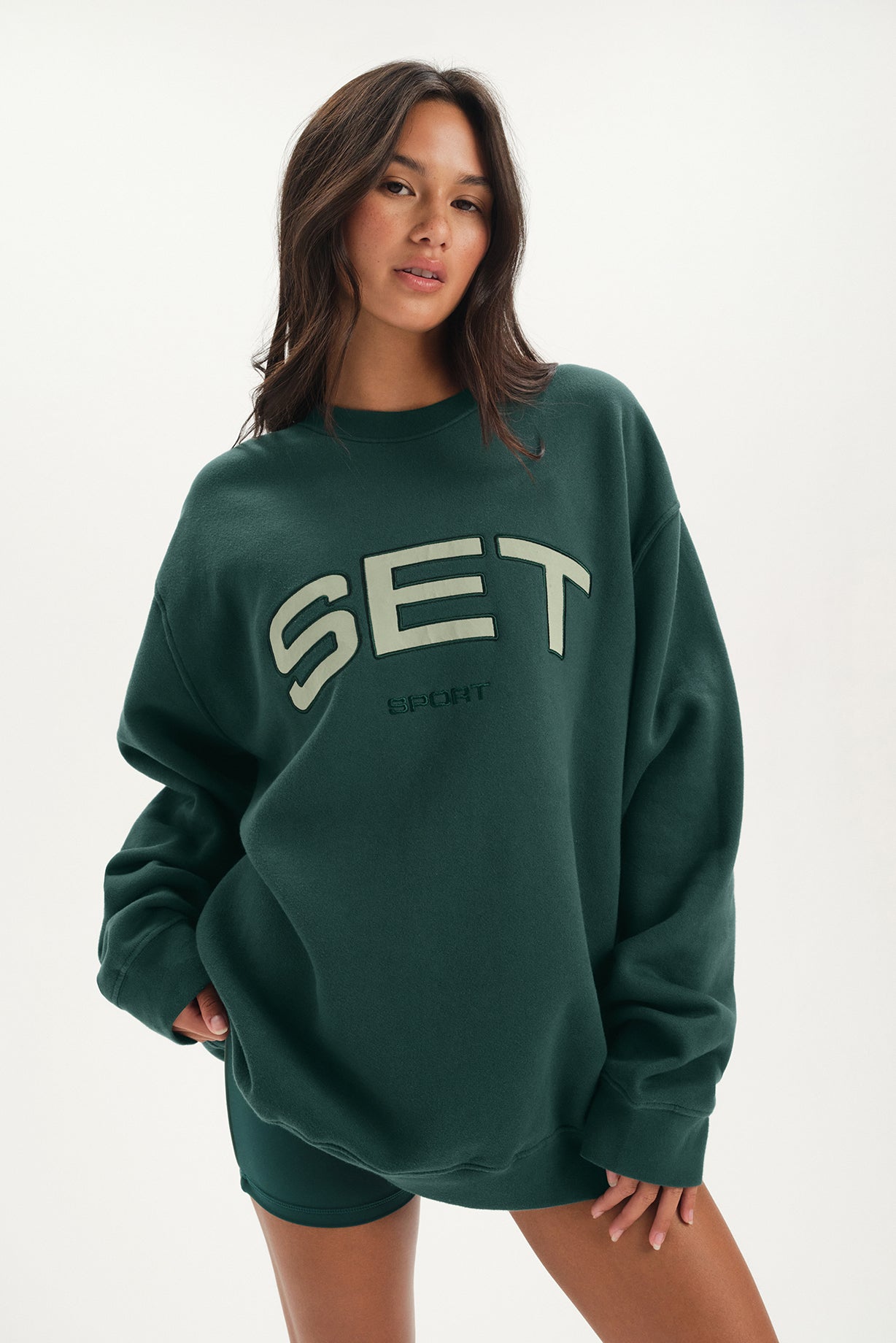 Person wearing a green sweatshirt with 'SET' text on a white background <model-info>Jelene wears a size L and is 5’7”, 23” waist, 32AB bust.</model-info>