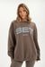 Woman wearing a brown sweatshirt with 'SET Sport' logo on a white background <model-info>Bre wears a size L and is 5’7”, 25½" waist, 33” bust.</model-info>