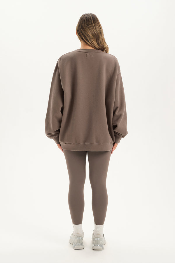 Person wearing a brown sweatshirt and leggings set on a white background