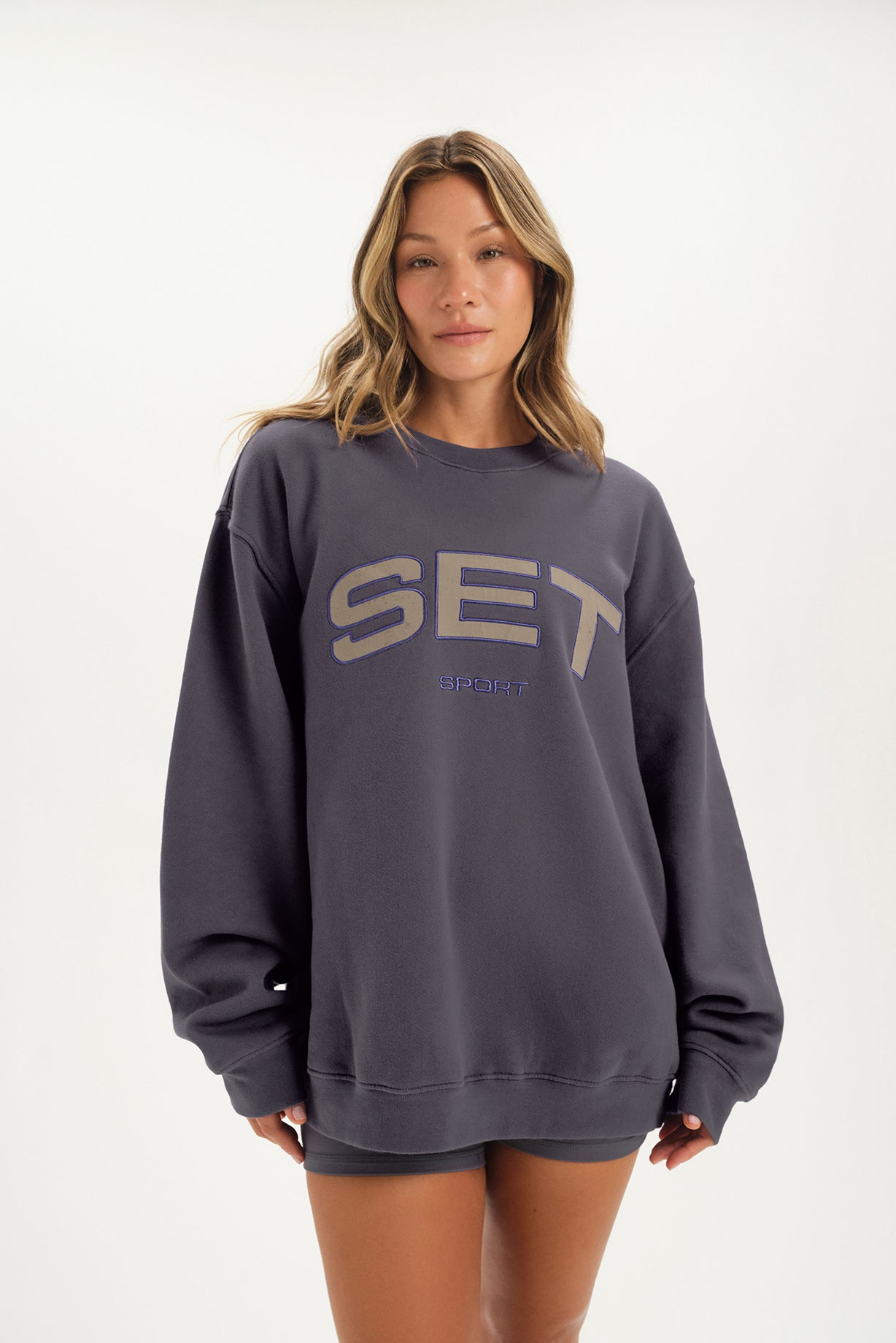 Woman wearing a dark gray sweatshirt with 'SET' text on a white background <model-info>Bre wears a size L and is 5’7”, 25½" waist, 33” bust.</model-info>