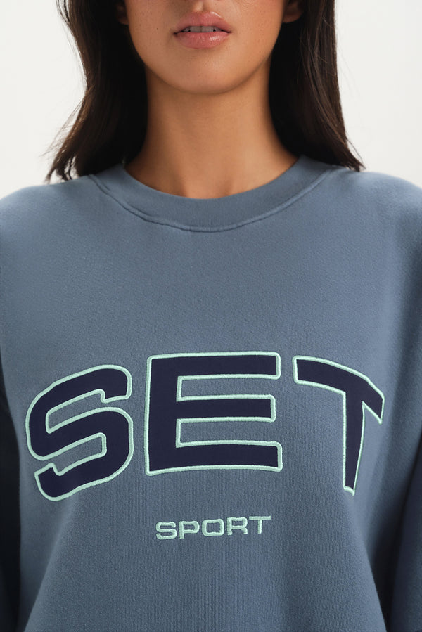 Gray sweatshirt with 'SET Sport' text worn by a person