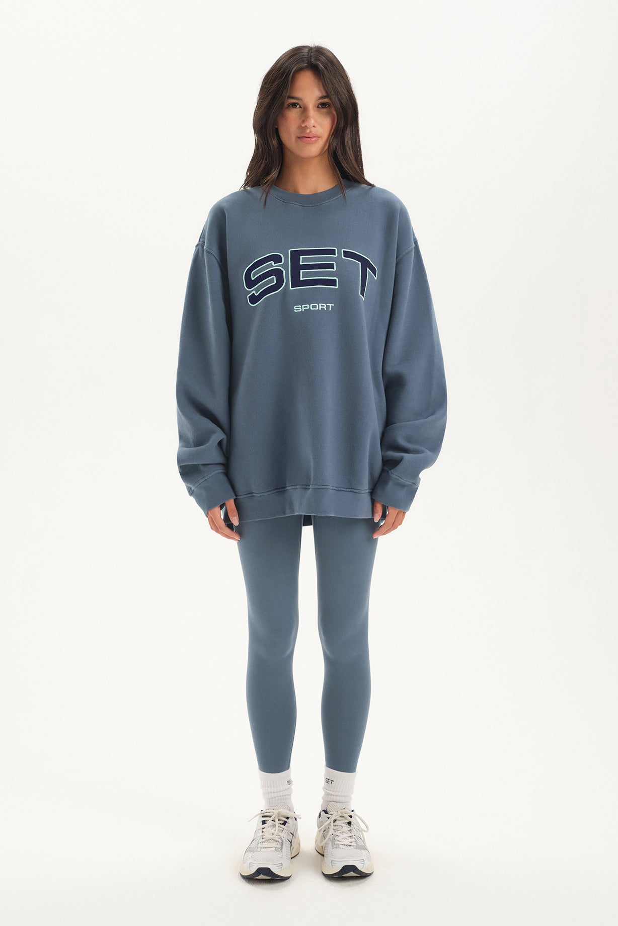 Person wearing a blue 'SET' sweatshirt and leggings on a white background