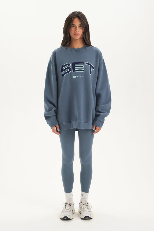 Person wearing a blue 'SET' sweatshirt and leggings on a white background
