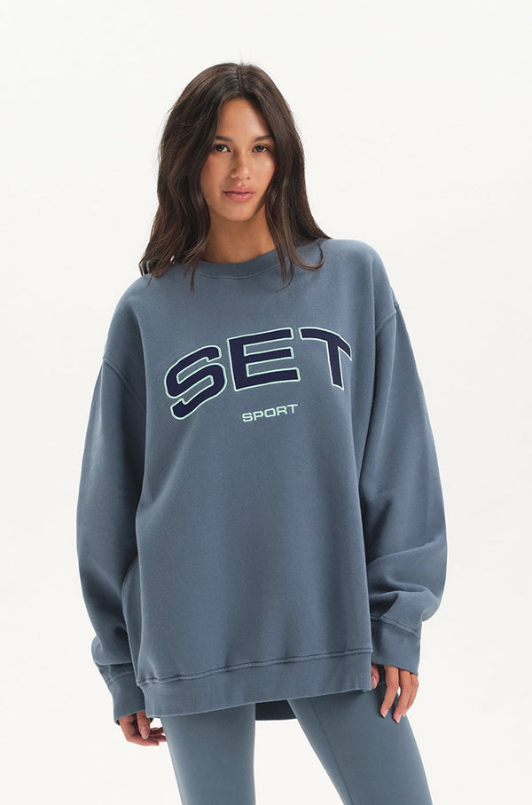 Woman wearing a blue 'SET Sport' sweatshirt on a white background 