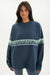 Woman wearing a blue sweater with a brand logo on a white background <model-info>Jelene wears a size XS and is 5’7”, 23” waist, 32AB bust.</model-info>
