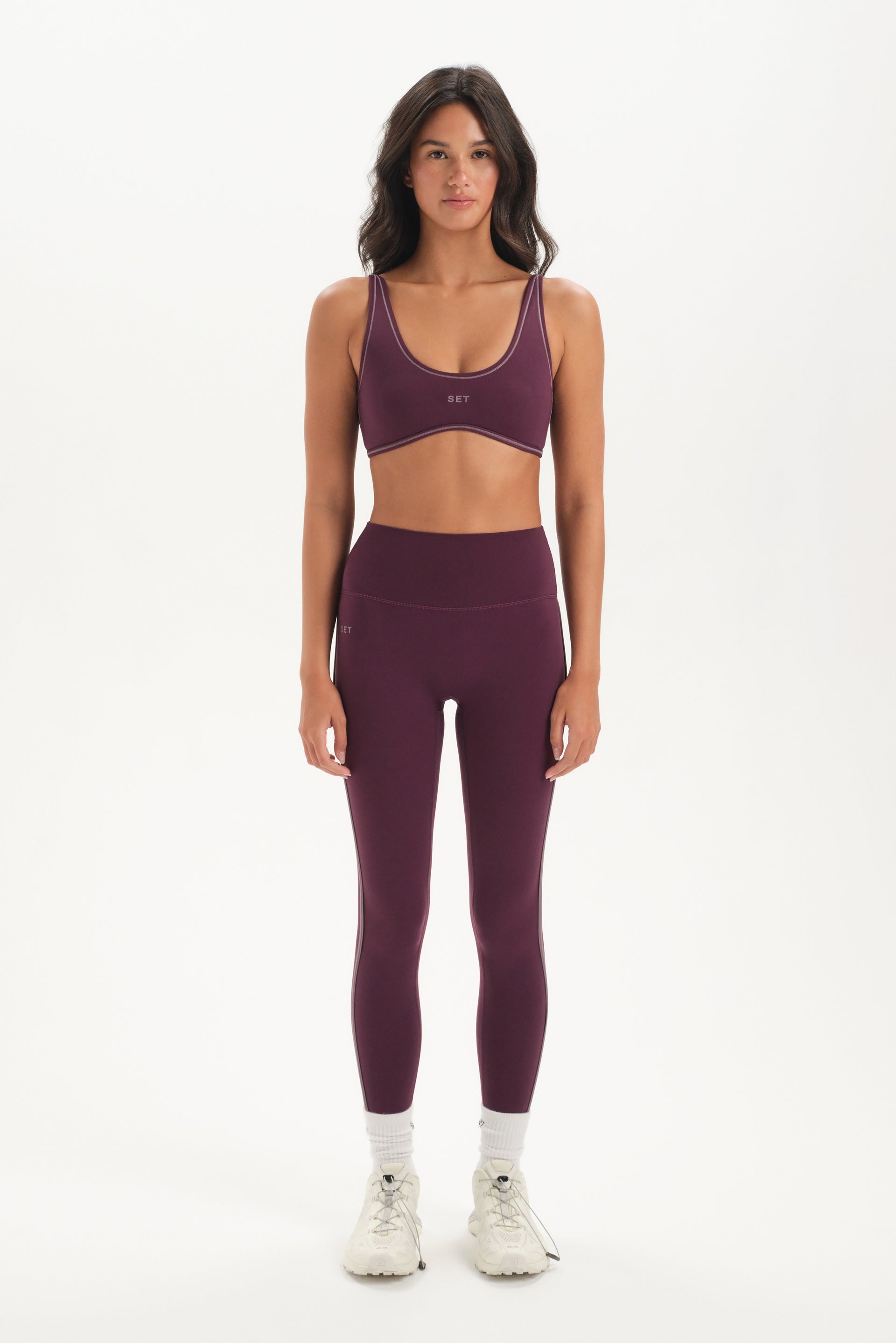 Woman wearing a purple sports bra and leggings set on a white background