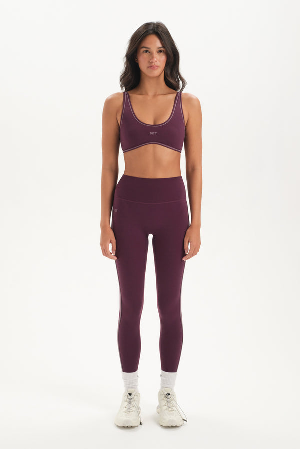 Woman wearing a purple sports bra and leggings set on a white background