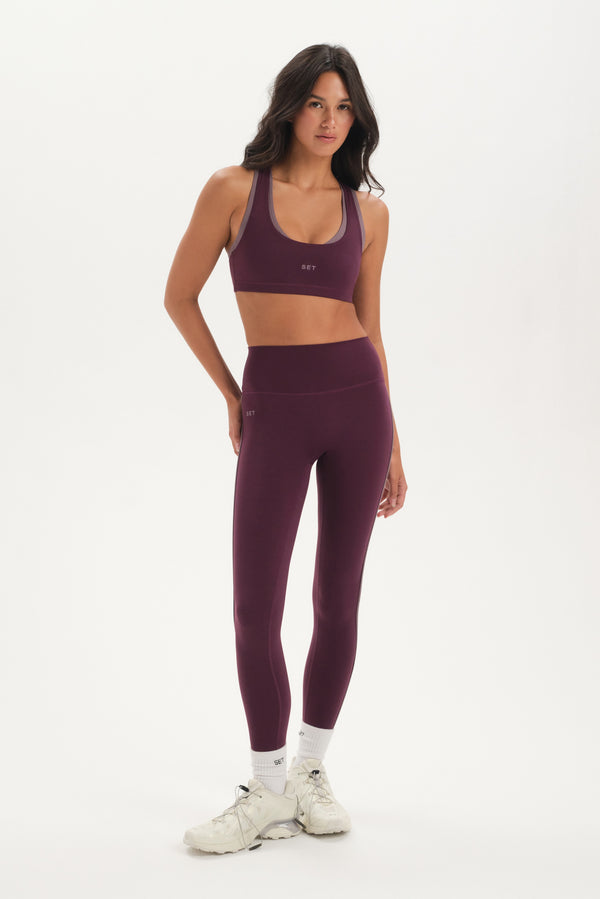 Woman wearing a purple sports bra and leggings set on a white background