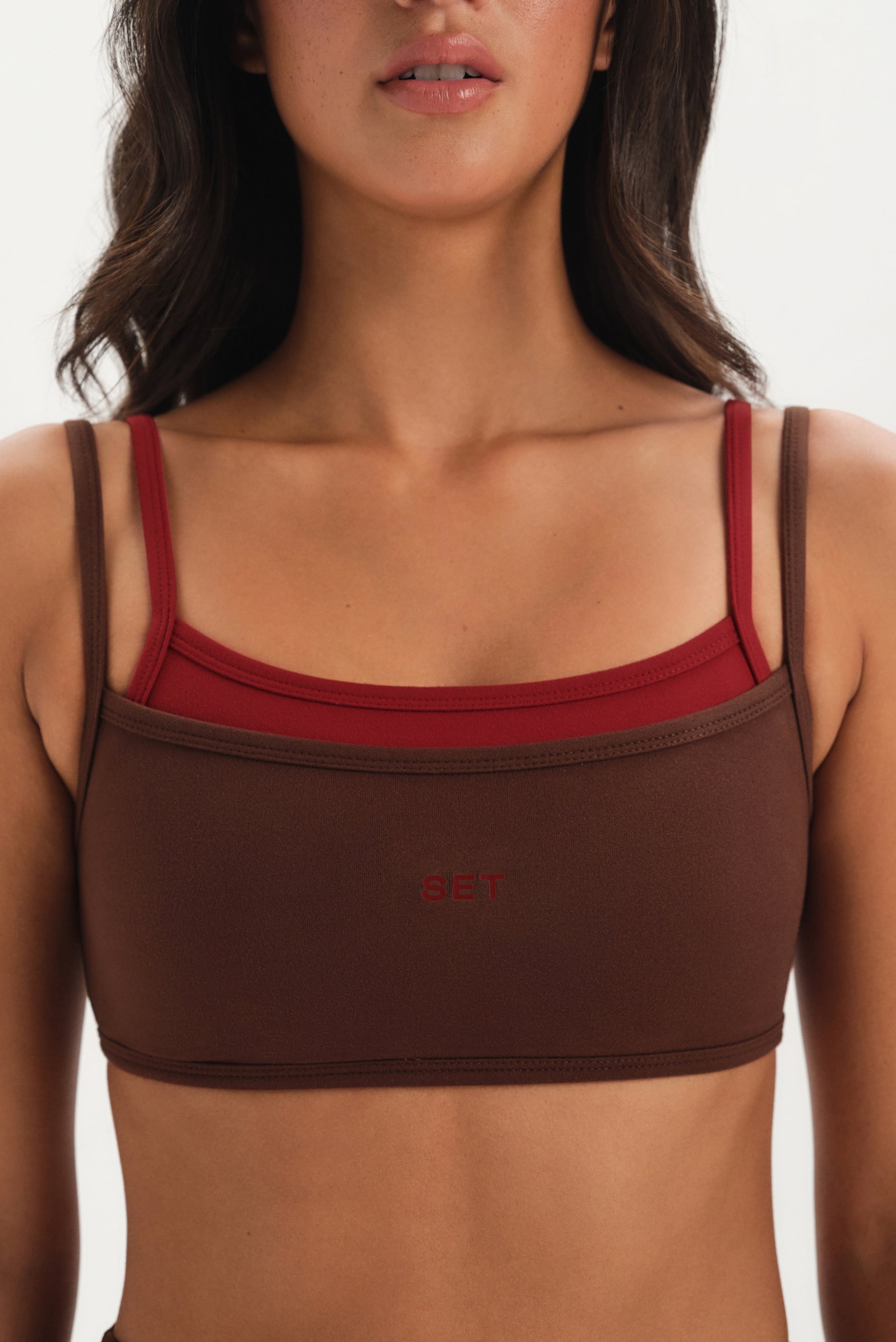 Brown sports bra with red accents worn by a model on a white background
