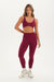 Woman wearing a maroon sports bra and leggings set on a white background