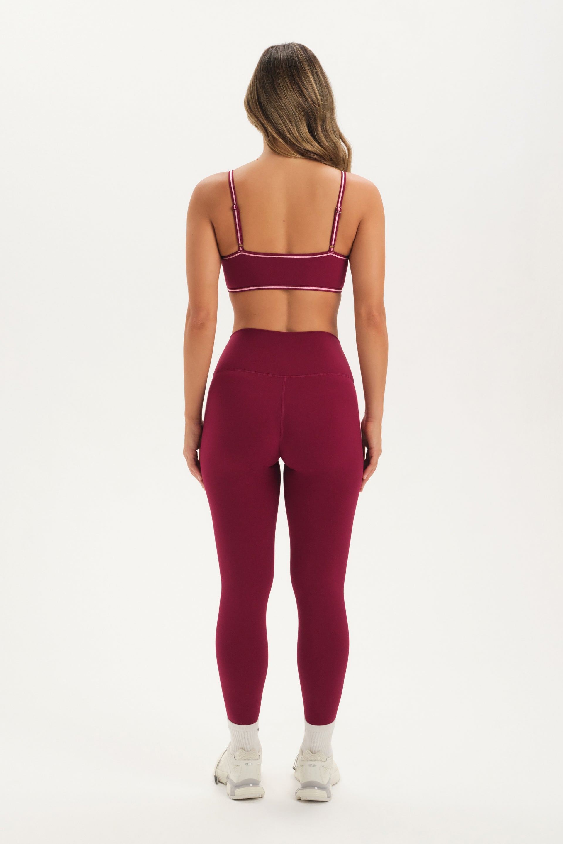 Woman wearing a maroon sports bra and leggings set on a white background