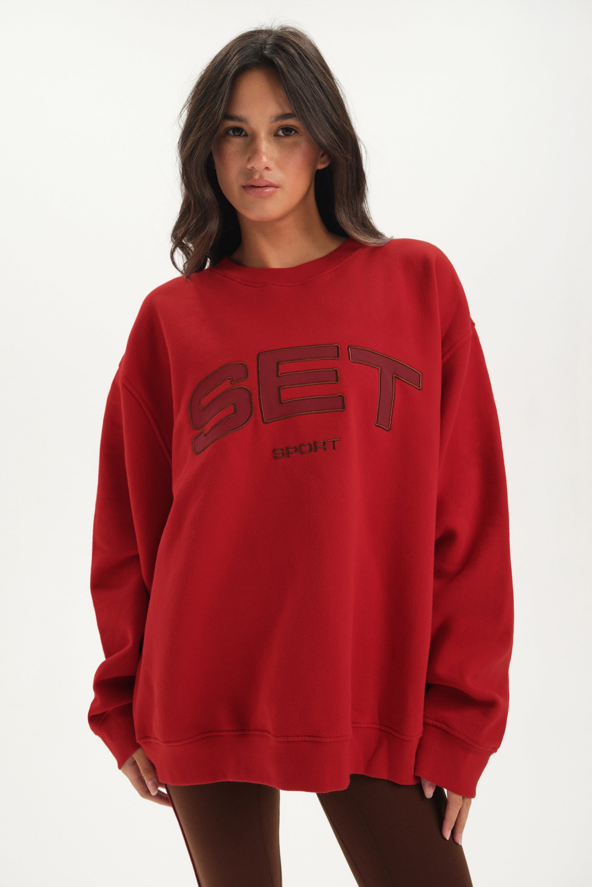 Woman wearing a red sweatshirt with 'SET' logo on a white background <model-info>Jelene wears a size L and is 5’7”, 23” waist, 32AB bust.</model-info>