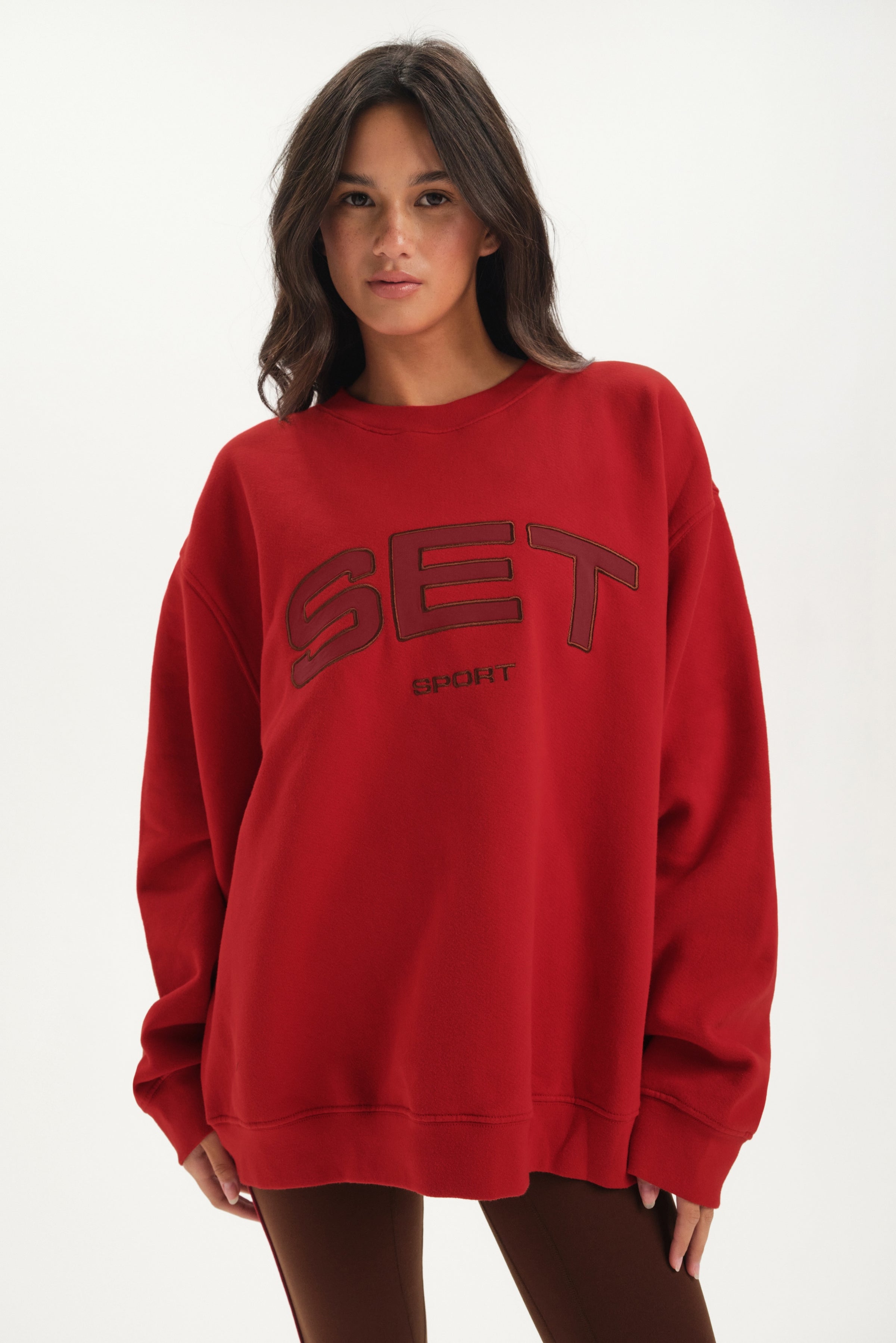 Woman wearing a red sweatshirt with 'SET' logo on a white background 