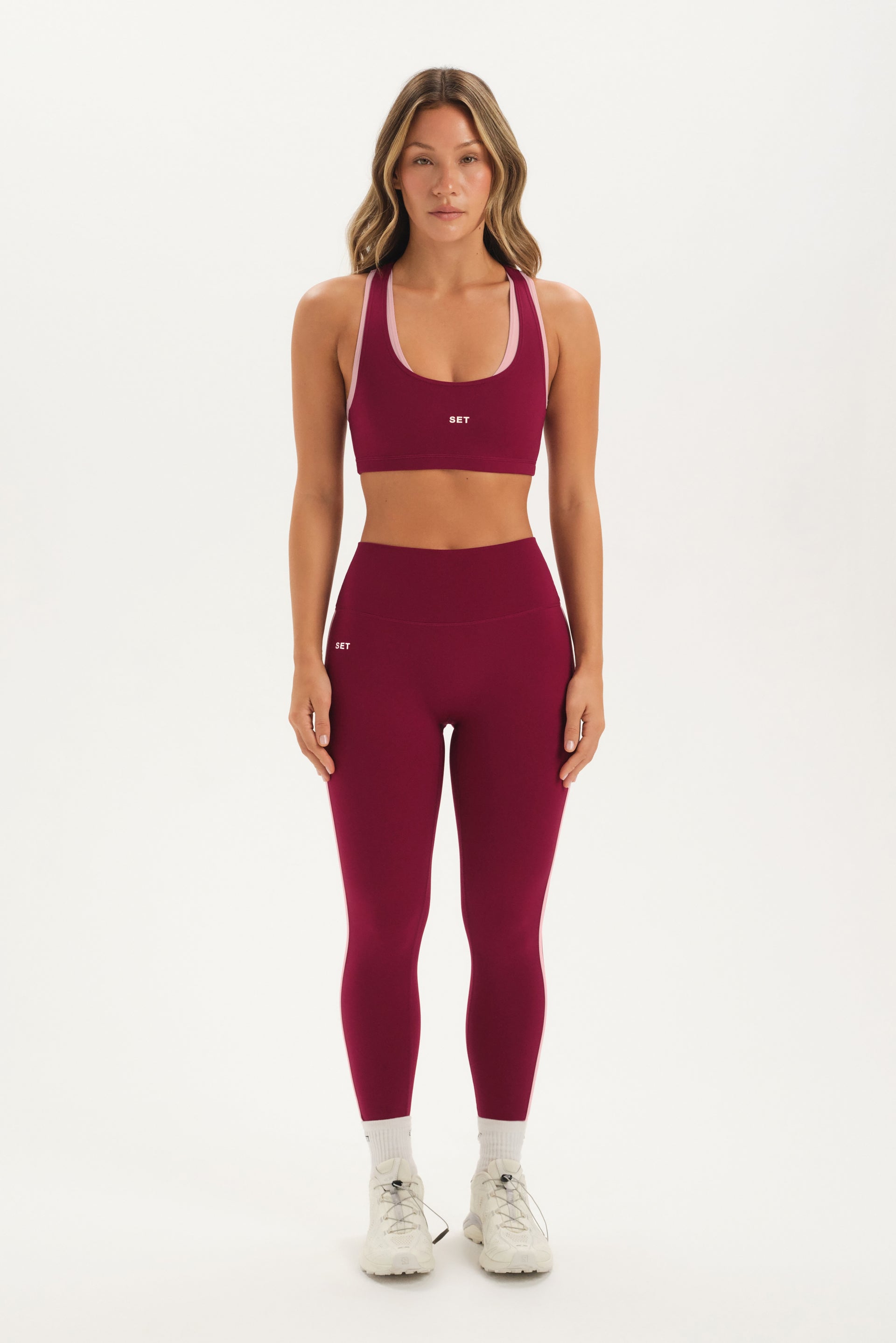 Woman wearing a maroon sports bra and leggings set on a white background