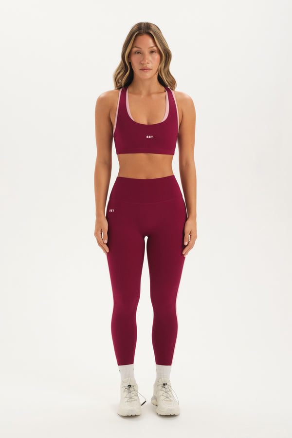Woman wearing a maroon sports bra and leggings set on a white background