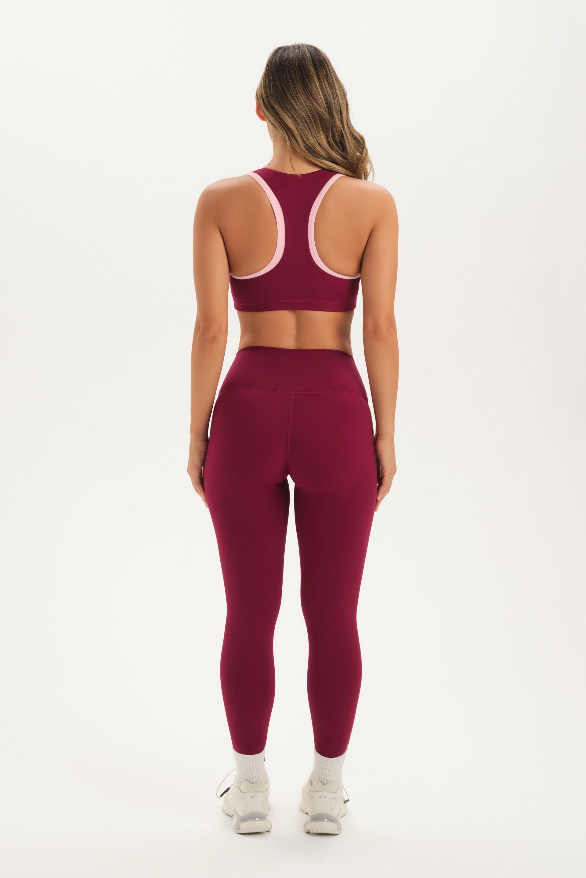 Woman wearing a maroon sports bra and leggings set on a white background