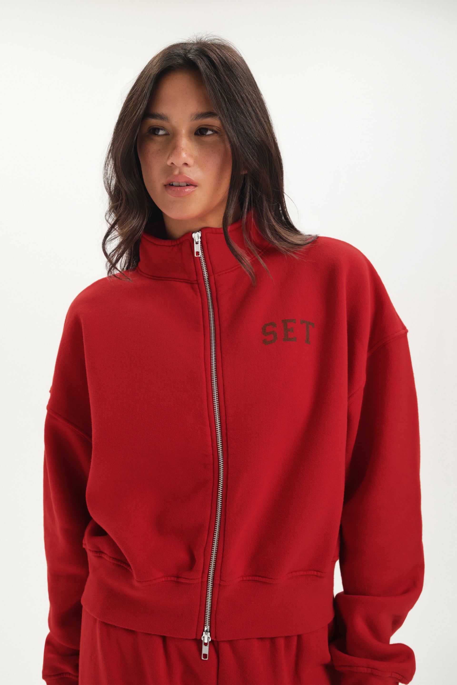 Person wearing a red zip up with 'SET' branding on a white background <model-info>Jelene wears a size S and is 5’7”, 23” waist, 32AB bust.</model-info>