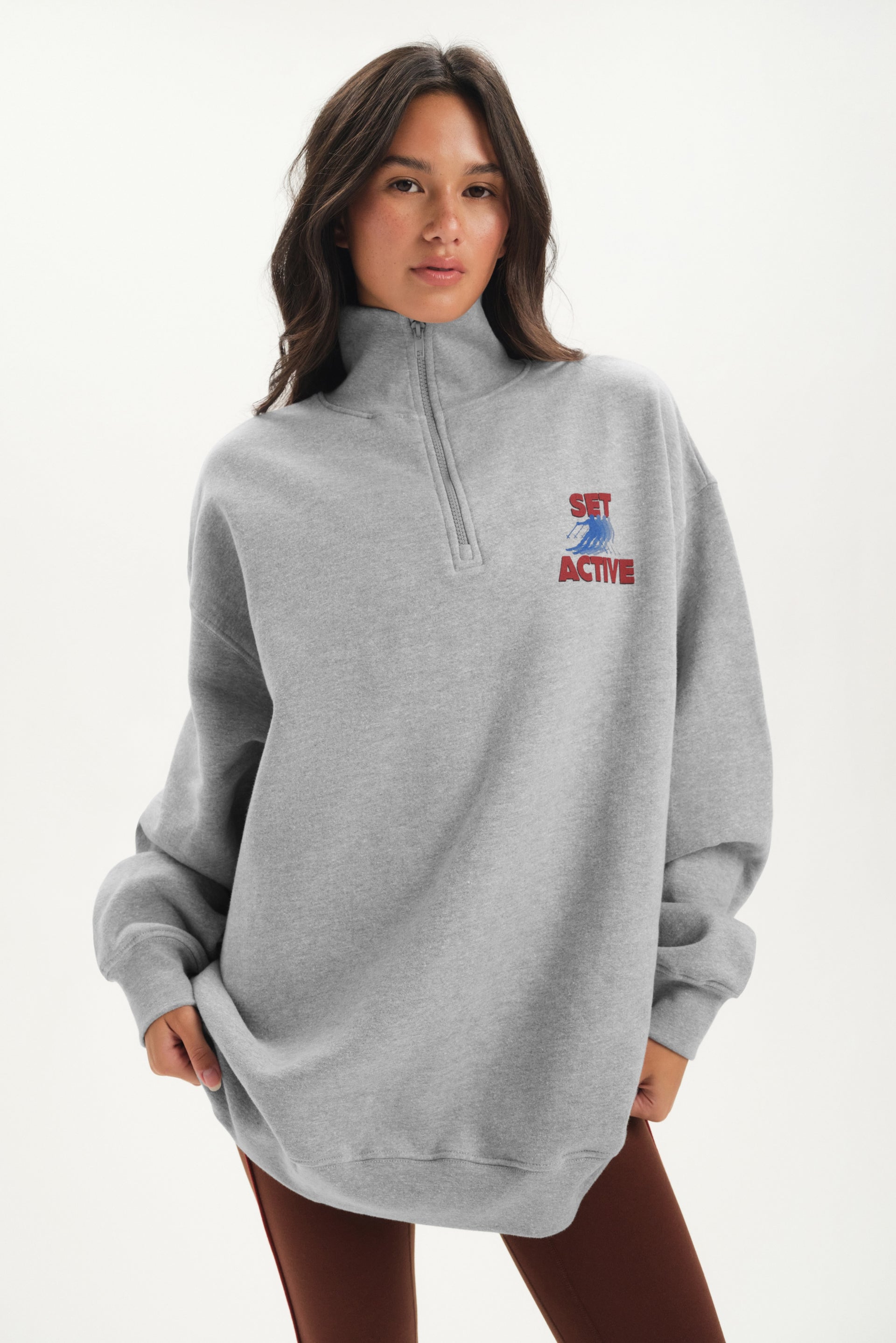 Person wearing a gray sweatshirt with a logo on a white background <model-info>Jelene wears a size M and is 5’7”, 23” waist, 32AB bust.</model-info>
