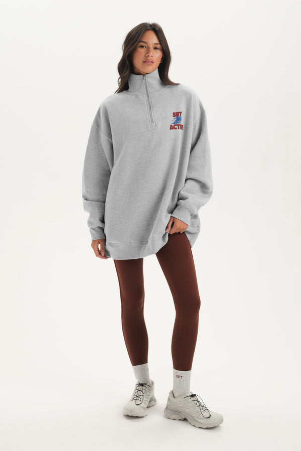 Person wearing a gray oversized sweatshirt with a logo on a white background