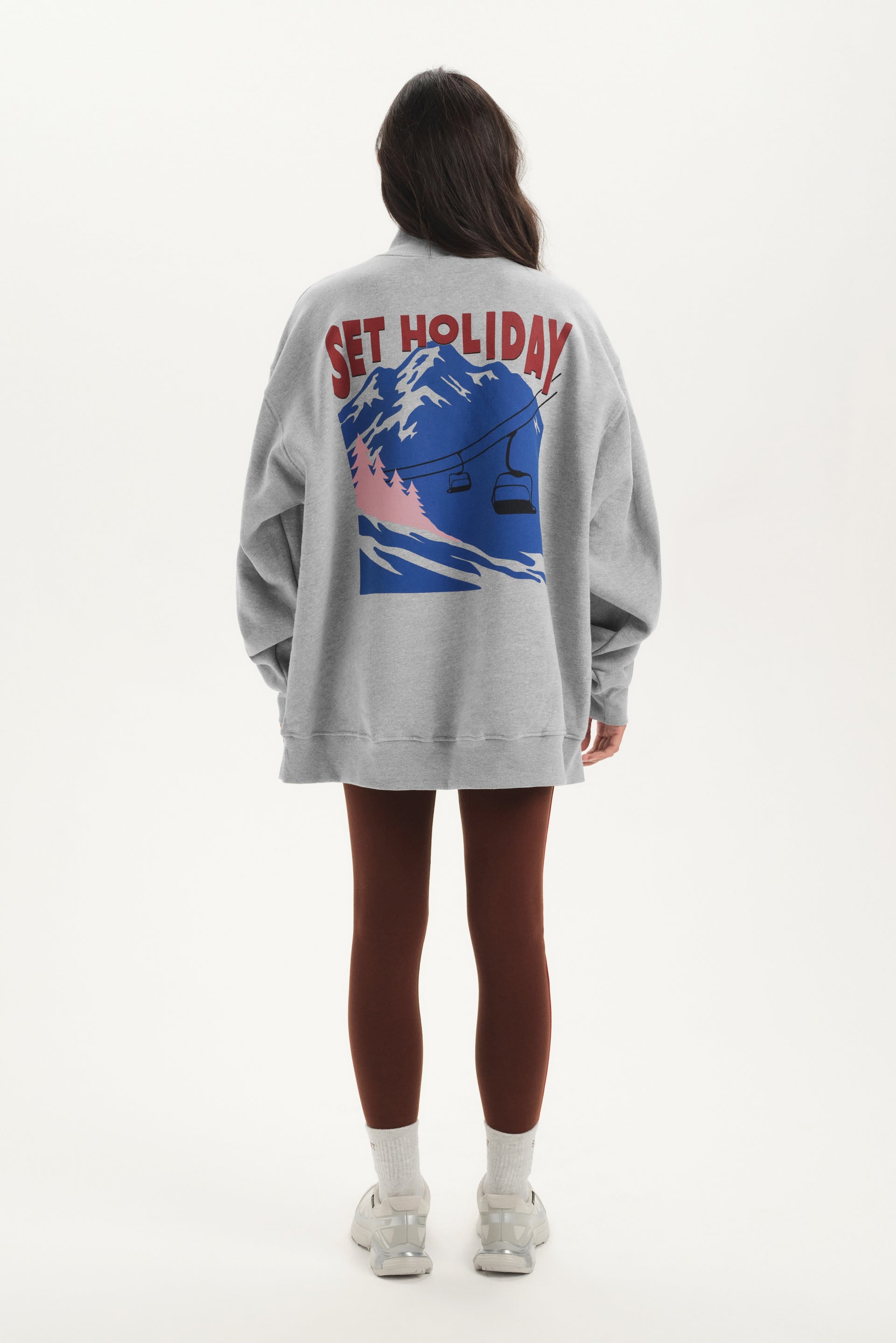 Person wearing a gray sweatshirt with a graphic design on the back, standing against a white background