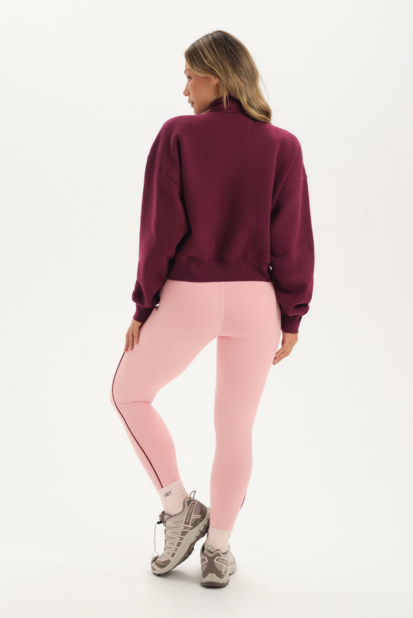 Woman wearing a maroon sweatshirt and pink leggings on a white background