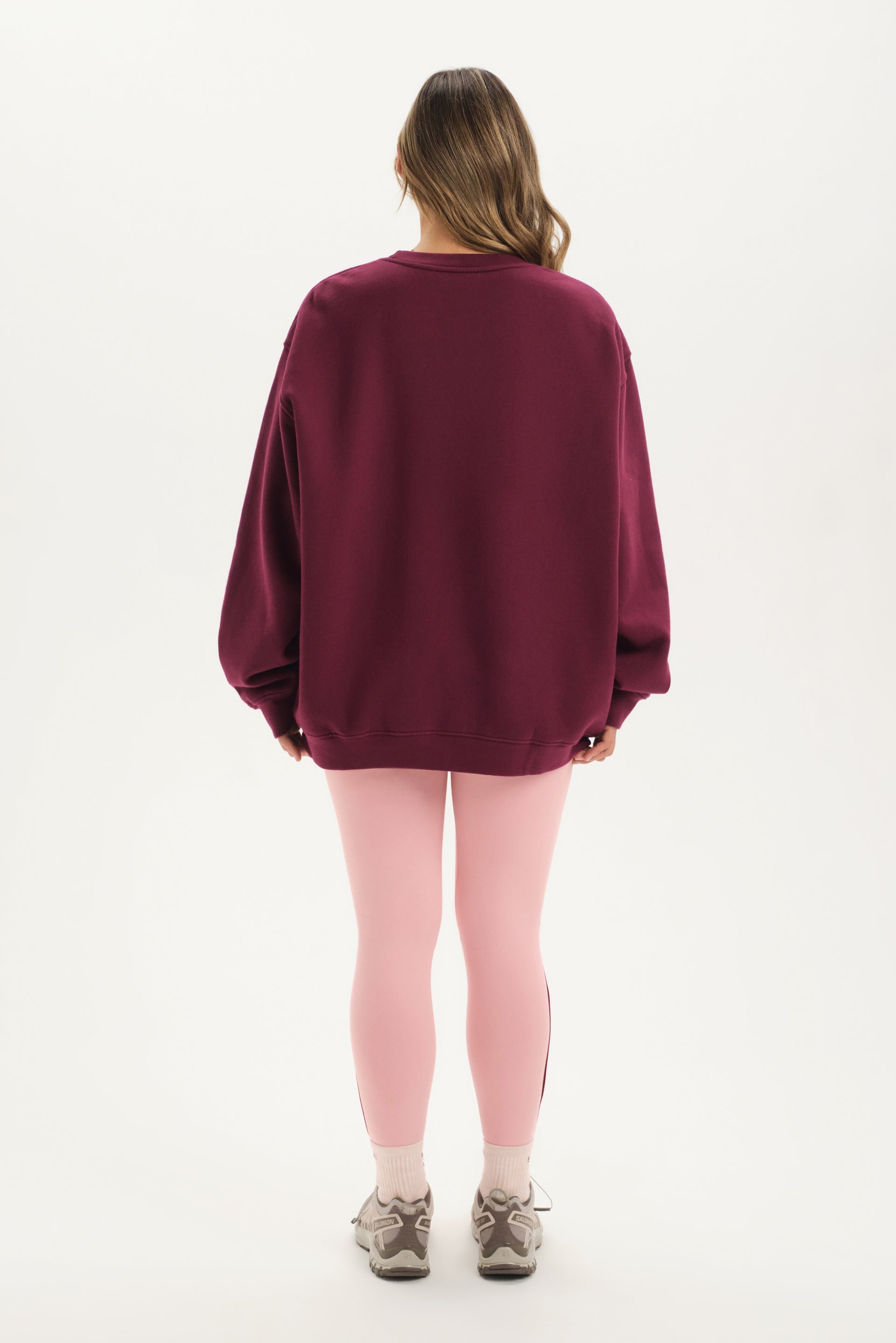 Person wearing a maroon oversized sweatshirt and pink leggings on a white background
