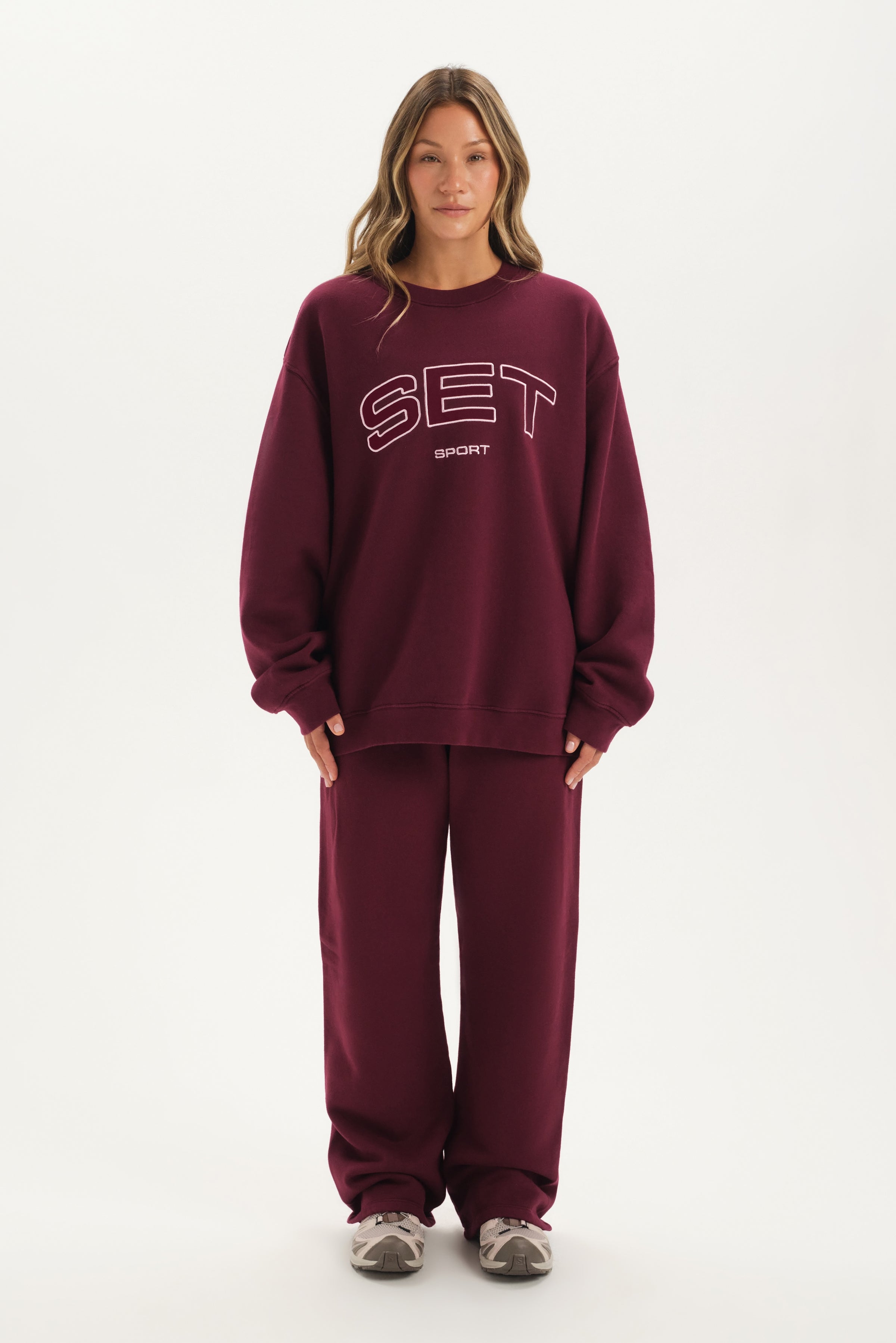 Person wearing a maroon 'SET' sweatshirt and pants on a white background