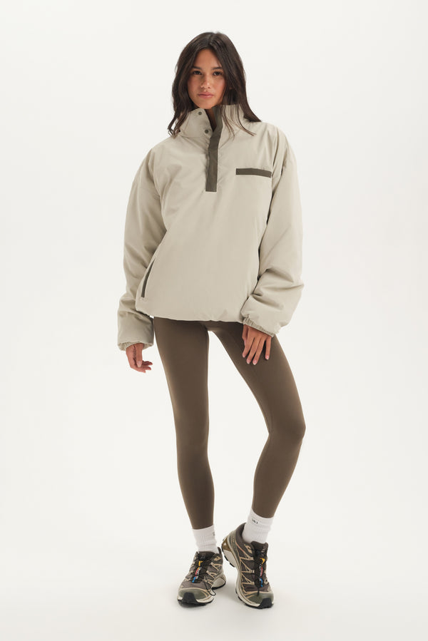 Woman wearing a beige jacket and brown leggings on a white background